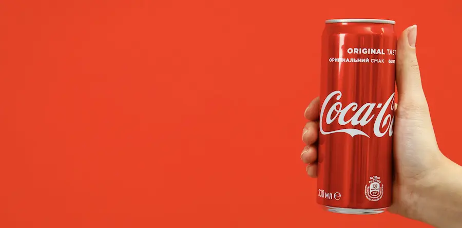 mano con una lata de Coca-Cola y fondo rojo